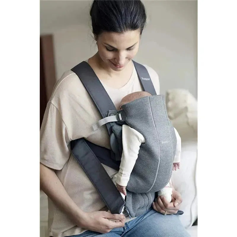 BabyBjorn Baby Carrier Mini in Dark Gray, featuring a woman holding an infant snugly in a soft, ergonomic design.