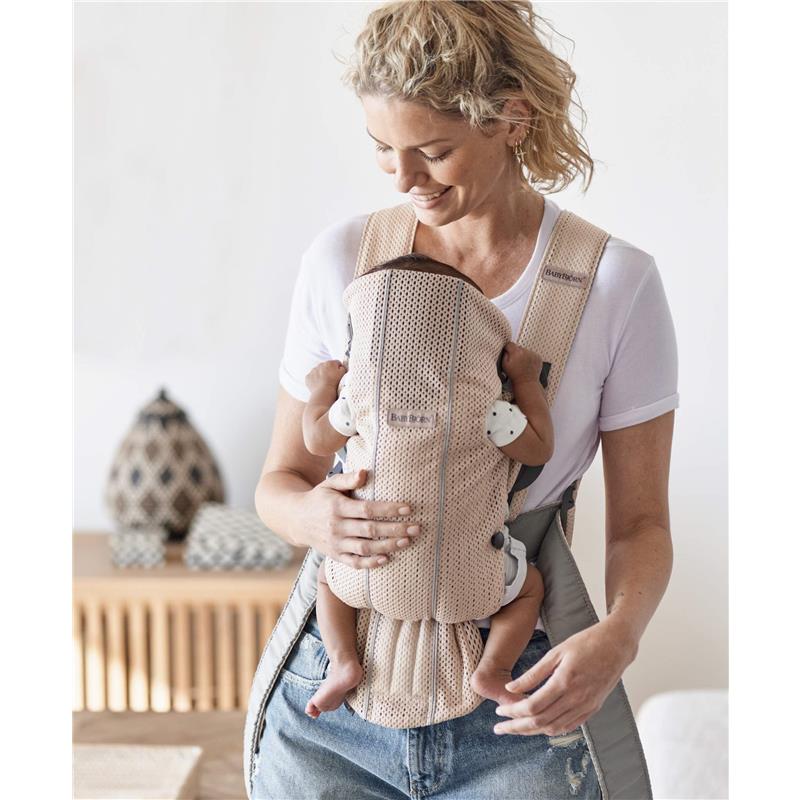 Woman holding a baby in a BabyBjörn Baby Carrier Mini, featuring a 3D mesh design in Pearly Pink color.