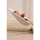 Light beige BabyBjörn Bouncer Balance Soft with a baby in a cozy sweater, comfortably seated and reaching out.