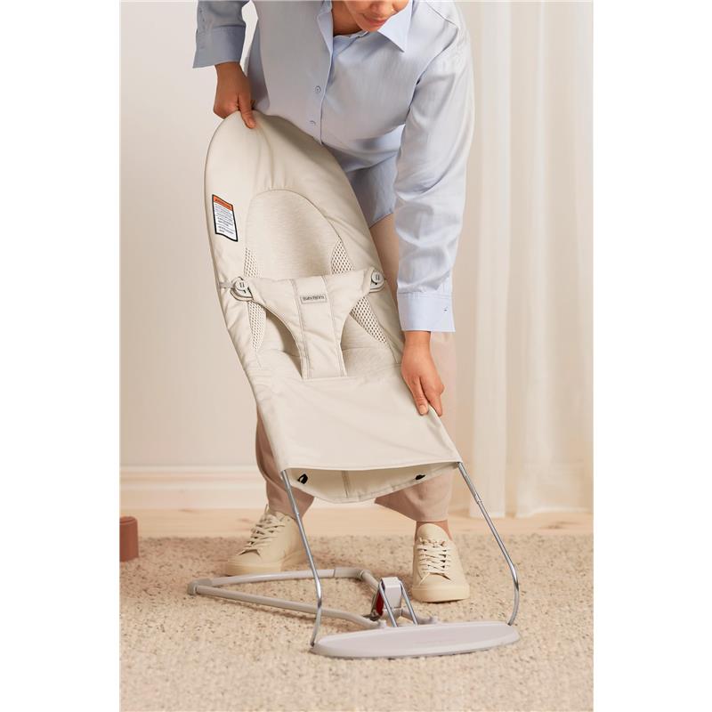 Adult adjusting the BabyBjörn Bouncer Balance Soft in light beige, highlighting its adjustable design and safety features.
