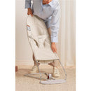Adult adjusting the BabyBjörn Bouncer Balance Soft in light beige, highlighting its adjustable design and safety features.
