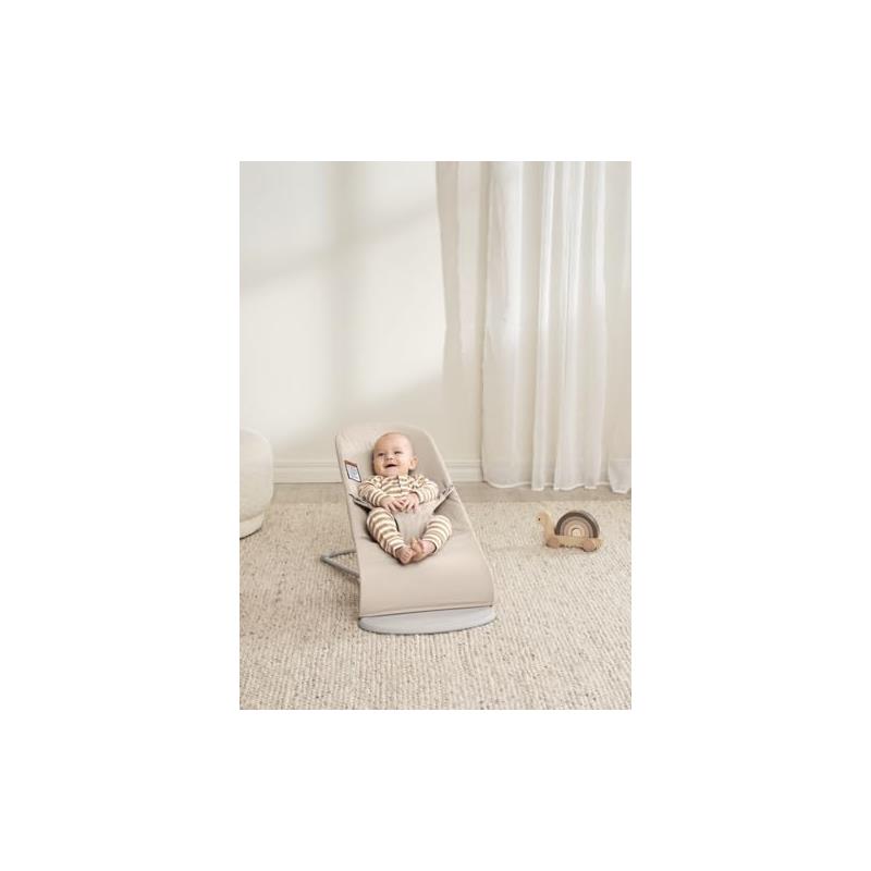 Babybjorn Bouncer Bliss in light beige with a smiling baby wearing striped clothing, lounging on a soft surface.