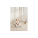 Babybjorn Bouncer Bliss in light beige with a smiling baby wearing striped clothing, lounging on a soft surface.