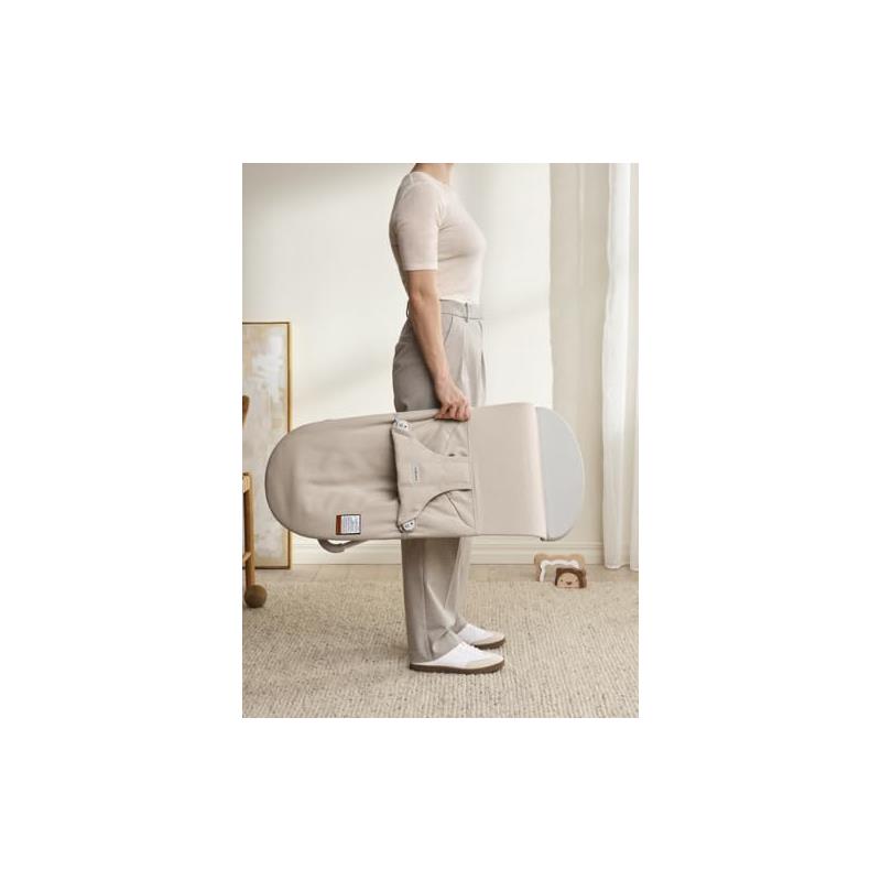 Light beige Babybjorn Bouncer Bliss being carried by a person in casual attire, showcasing its portable design.