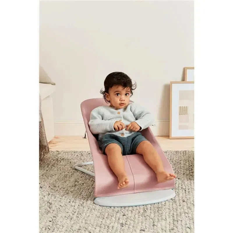 Babybjorn Bouncer Bliss in Dusty Pink, featuring a seated child wearing a gray cardigan and shorts on a soft rug.