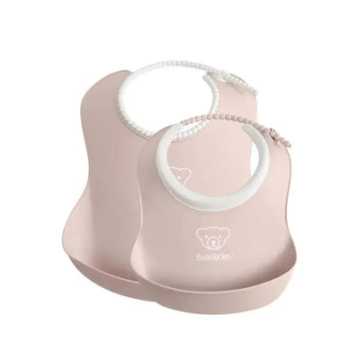 Two Babybjorn feeding bibs in powder pink, featuring a soft design and a bear logo, ideal for mealtime use.
