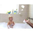 A surprised toddler in a bubble bath plays with bath toys while bubbles float around. Babyganics products are visible in the background.