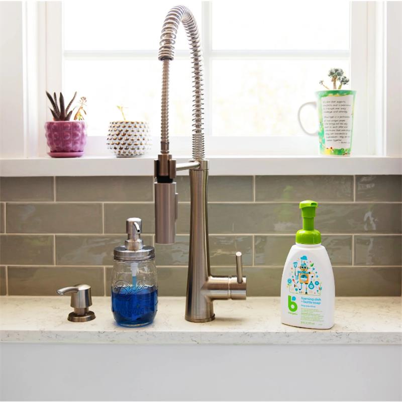 Foaming Dish + Bottle Soap from Babyganics, 16 oz, displayed on a kitchen countertop beside a modern faucet and blue liquid soap dispenser.