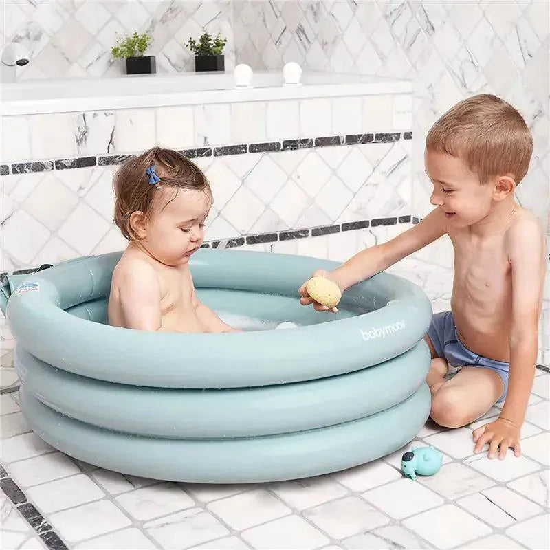 Inflatable Babymoov bathtub with a baby seated inside, while a young boy smiles and plays with a toy beside them.