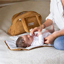 Changing a baby on a white mat while a camel-colored Bbluv changing bag is visible in the background.