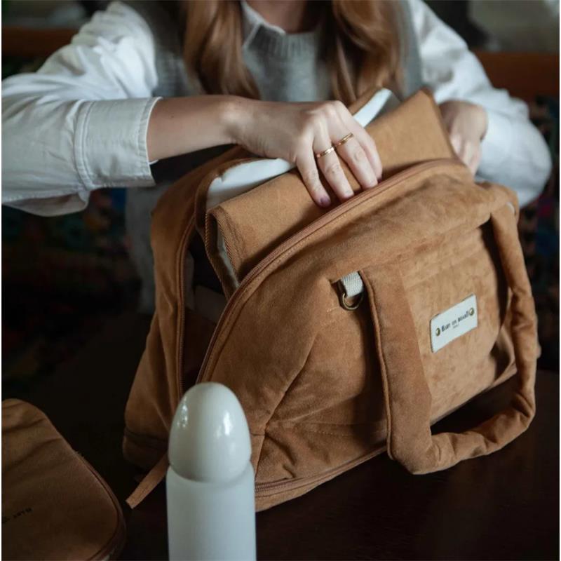 Doudoune changing bag by Bbluv in camel color, with a person unpacking items from it on a table.