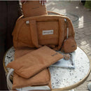 Camel-colored Bbluv Doudoune Changing Bag displayed on a table with matching accessories, including a changing mat and small pouch.