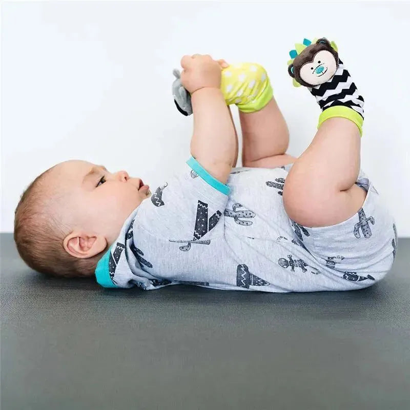 Baby lying on back, holding Bbluv Duo Foot Finders socks featuring a hedgehog and raccoon, engaging with colorful toy designs.