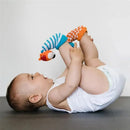 A baby lying on their back plays with Bbluv Duo Foot Finders, featuring owl and fox designs on colorful sock attachments.