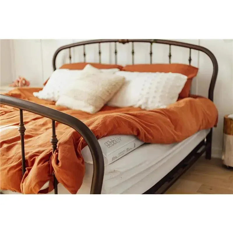 Inflatable bed bumpers on a white mattress, with an orange duvet, pillows, and a black metal bed frame.