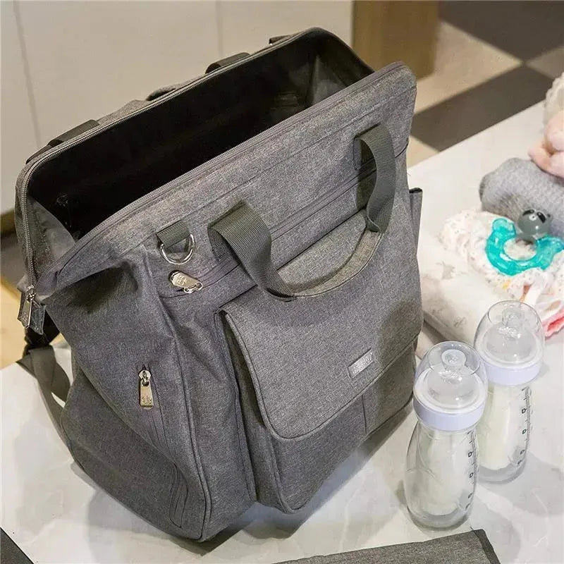 Charcoal Bbluv Metrö Complete Backpack Diaper Bag with a zipper closure, side pockets, and two baby bottles nearby.