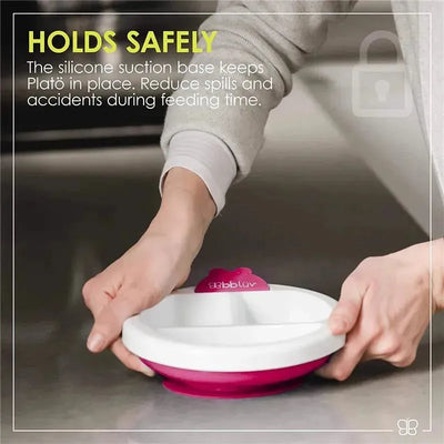 Pink Bbluv Platö Warm Feeding Plate with silicone suction base, held by a person, designed to reduce spills during feeding.
