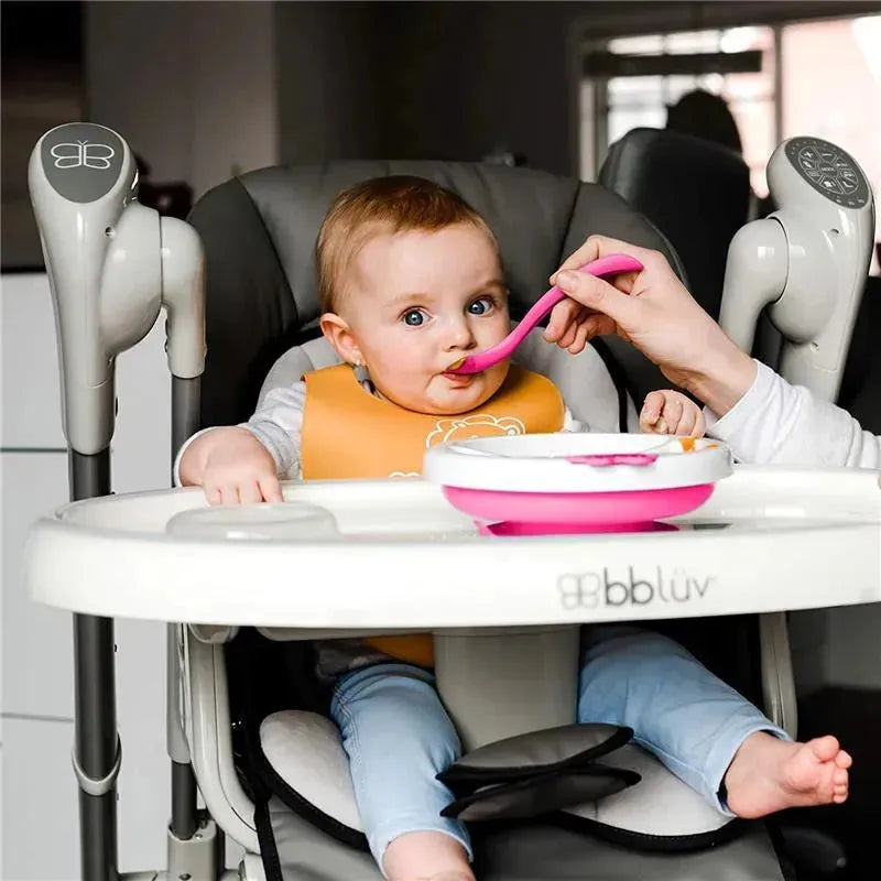 Baby in a high chair being fed with a pink spoon, using a Bbluv pink warm feeding plate.