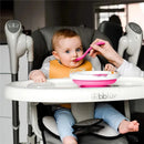Baby in a high chair being fed with a pink spoon, using a Bbluv pink warm feeding plate.