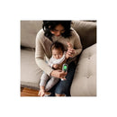 A woman sitting on a couch holds a Bbluv Termo 4-in-1 digital thermometer while caring for a baby.