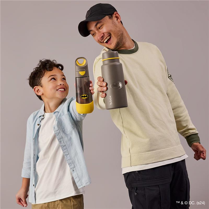 A child and an adult smile while holding two BBoox water bottles, one with a Batman design and one plain gray, in a light background.