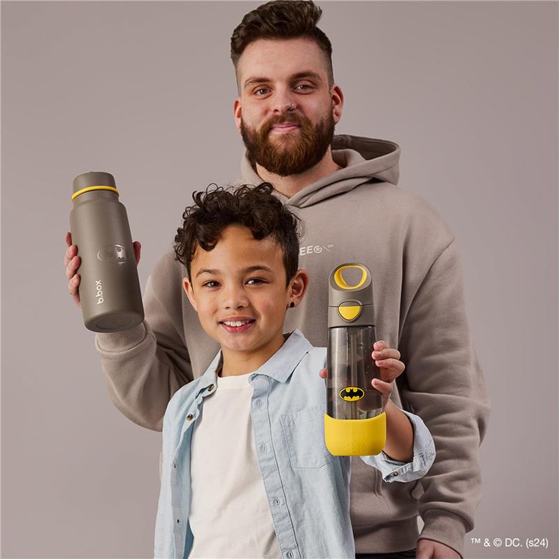Child smiling while holding a Batman-themed Tritan drink bottle, with an adult behind holding a gray BBoox water bottle.
