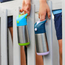 Insulated BBox water bottles in green and blue, held by children, displayed on a wooden fence.