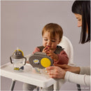Toddler seated in a high chair exploring a Batman-themed snackbox while an adult assists.