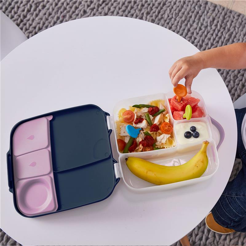 A child uses a Bbox Gel Cooler Twin Pack lunchbox filled with pasta, salad, fruit, yogurt, and a banana on a white table.
