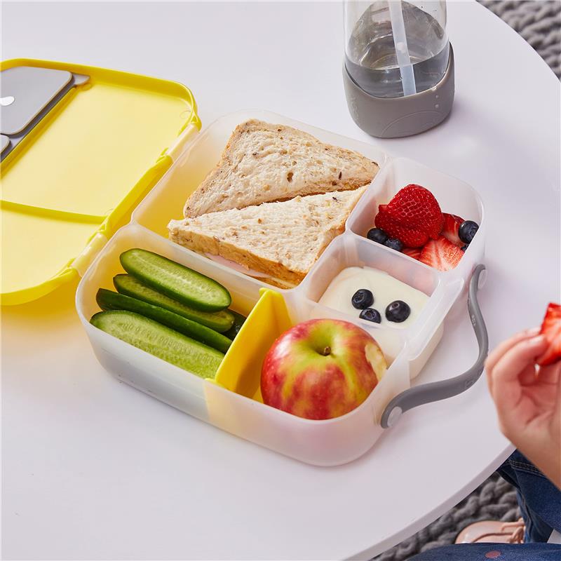 Lunchbox with compartments containing sandwiches, cucumber slices, an apple, yogurt with blueberries, and strawberries, beside a drink.