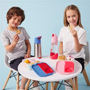 Two kids sitting at a table with a blue and red Bbox lunch box, snacks, and water bottles, smiling and enjoying their food.