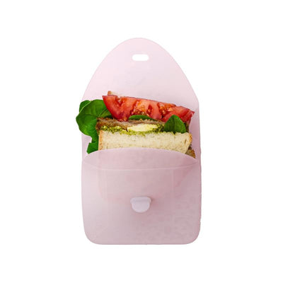 Silicone sandwich pocket in berry color, containing a sandwich with spinach, pesto, and tomato slices.