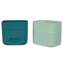 Silicone snack cups in forest colors, one teal and one light green, with a textured design for grip and aesthetic appeal.