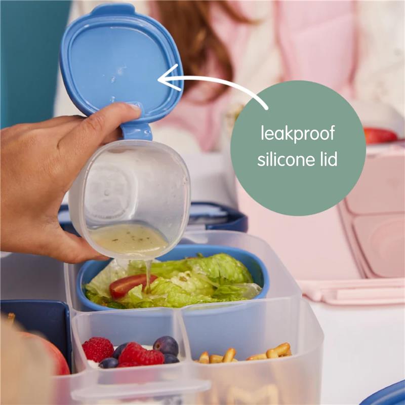 Bbox silicone snack tub with a leakproof blue lid pouring dressing over a salad, alongside fruits and snacks.