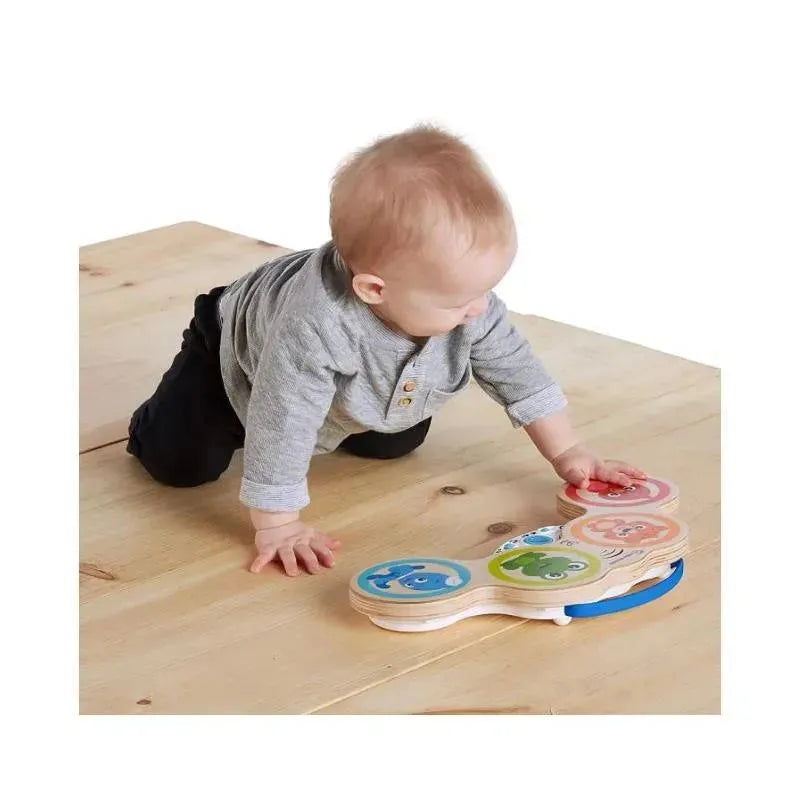 Baby playing with the Be Hape Magic Touch Drum, pressing colorful drum pads while on a wooden floor.