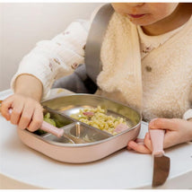A toddler uses a pink Beaba 3Pk stainless steel cutlery set to eat pasta and veggies from a divided plate.