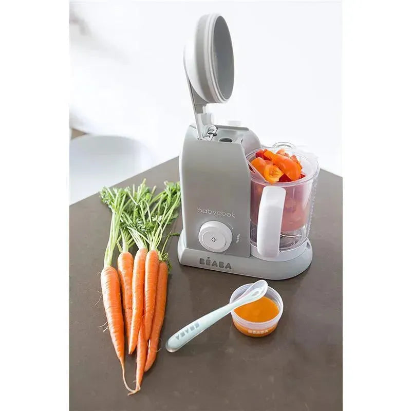 Beaba Babycook Solo 4 in 1 Baby Food Maker in cloud color, with chopped vegetables in the bowl, beside fresh carrots and a spoon with baby food.