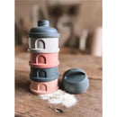 Beaba Formula and Snack Container in rose, stacked in four layers, with a light dusting of powder on a wooden surface.