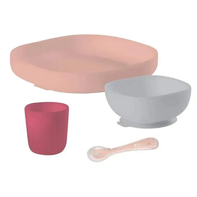 Four-piece silicone meal set in pink, including a pink plate, grey bowl, red cup, and pink spoon, ideal for children.