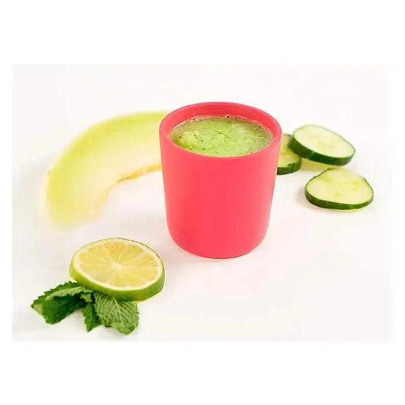 Silicone pink cup filled with green smoothie, surrounded by cucumber slices, lime, mint leaves, and a melon slice.