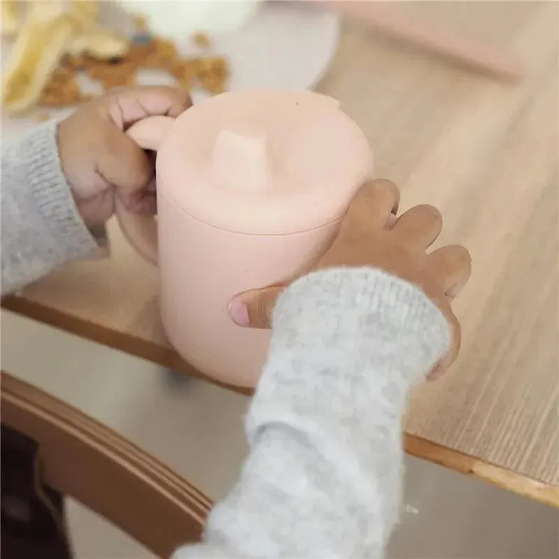 Silicone training cup in rose color held by a child, designed for easy grip during drinking.