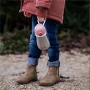 Stainless steel kids water bottle by Beaba in rose color, held by a child wearing a pink jacket and brown boots.