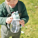 Beaba straw sippy cup in sage color held by a child, featuring a clear container and two handles.