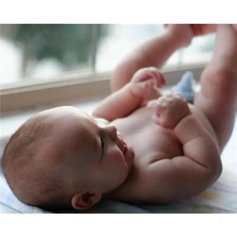 Baby lying on a blanket, enjoying playtime and reaching for a blue pee-pee teepee, smiling and looking up.