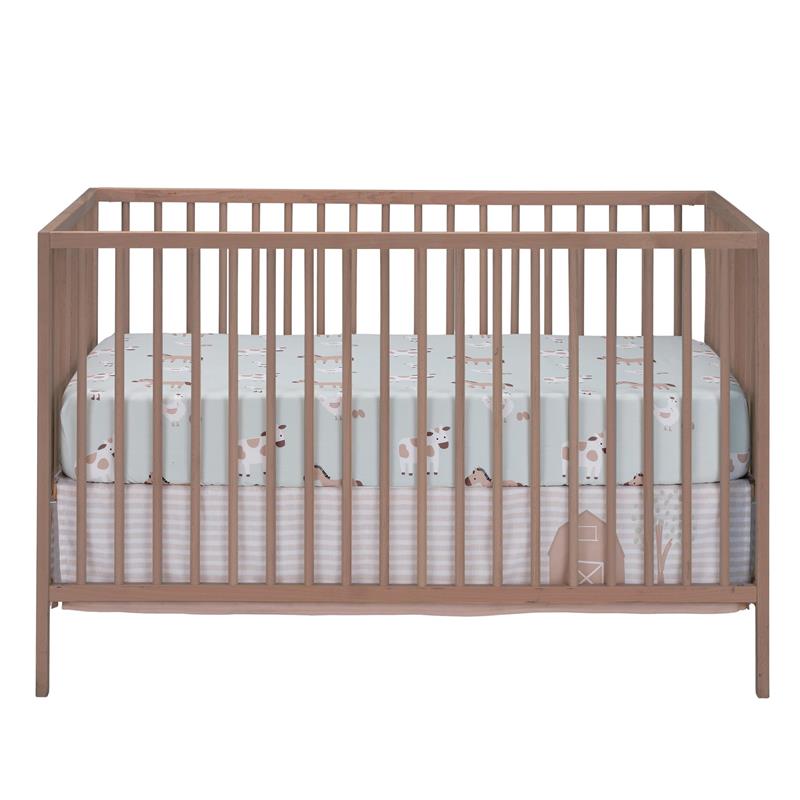 Nursery crib with a light blue bedding set featuring farm animal prints, including cows and a barn design.