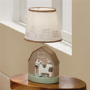 Decorative nursery lamp featuring a cow and bird design on a barn-shaped base with a soft-lit shade.