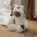 Plush cow stuffed animal toy with brown and white colors, sitting beside a blanket and a decorative basket.