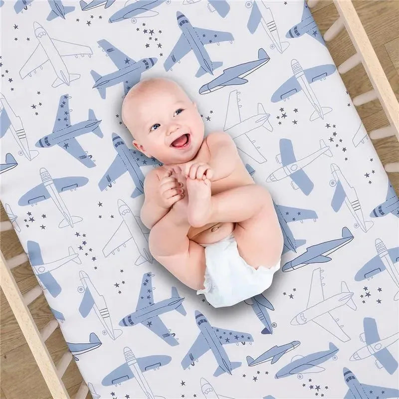 Smiling baby laying on a crib sheet featuring blue airplane patterns and stars, designed for infants.