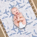 Smiling baby laying on a crib sheet featuring blue airplane patterns and stars, designed for infants.