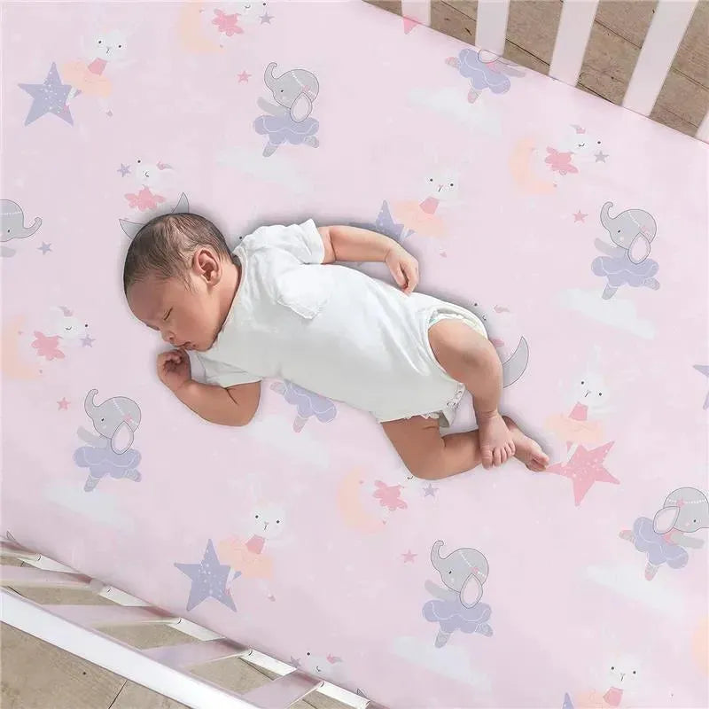 Fitted crib sheet featuring whimsical elephants and stars in pastel colors, with a sleeping baby dressed in white.